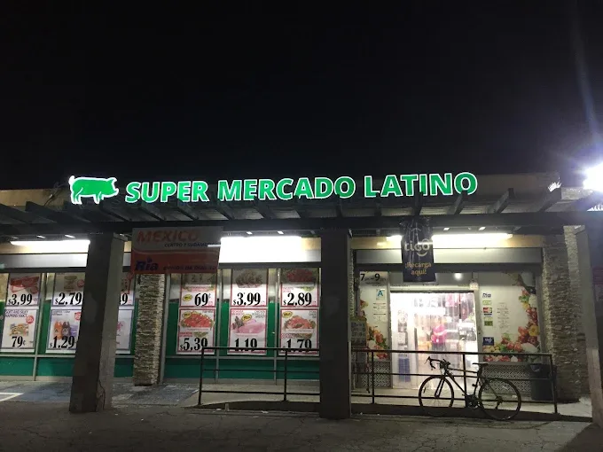 Fachada de Super Mercado Latino de noche, con el letrero verde iluminado